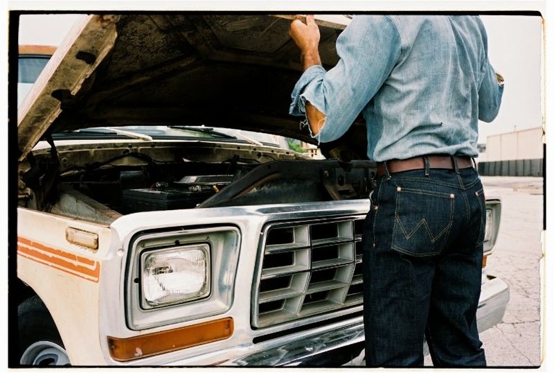 Close shot from behind a man opening the hood of a vintage truck.