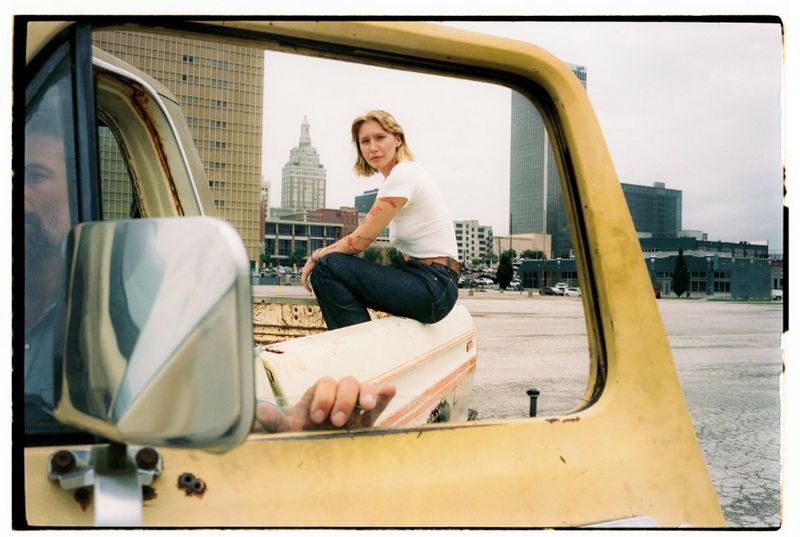 Woman sitting on the bed of a vintage truck, seen through an open truck door window.