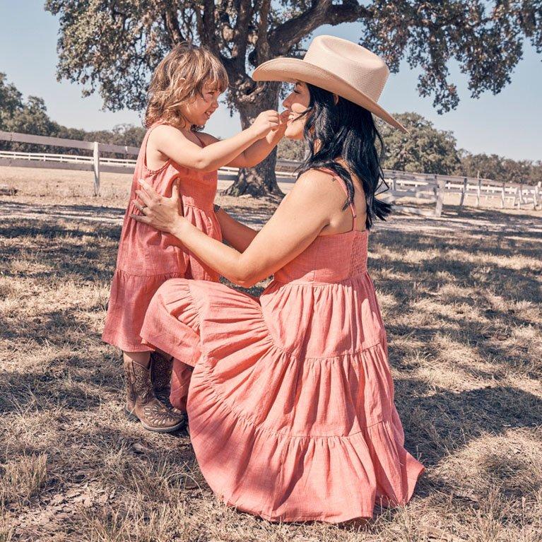 Mother and daughter in matching pink dresses, standing in a field