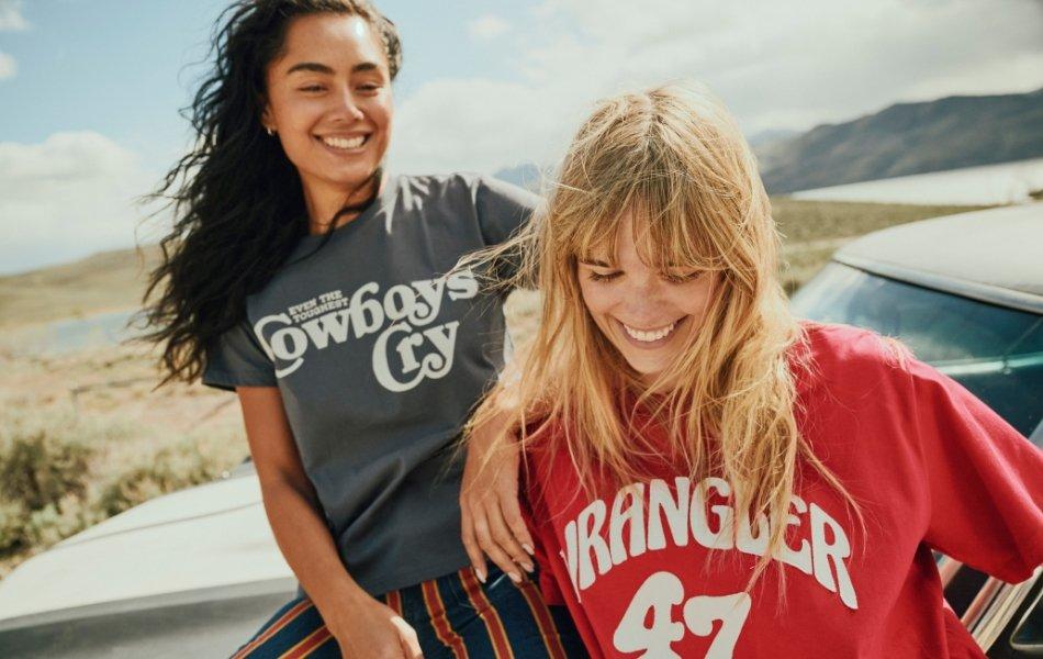 Two women leaning up against a car wearing Wrangler t-shirts.