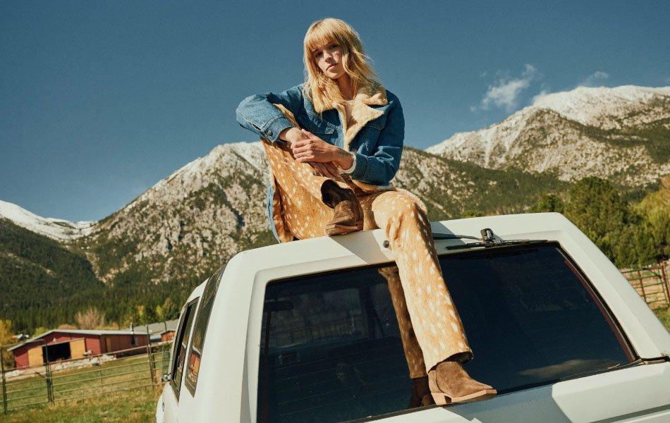 A girl sitting on the hood of a truck wearing a leopard print denim jacket.