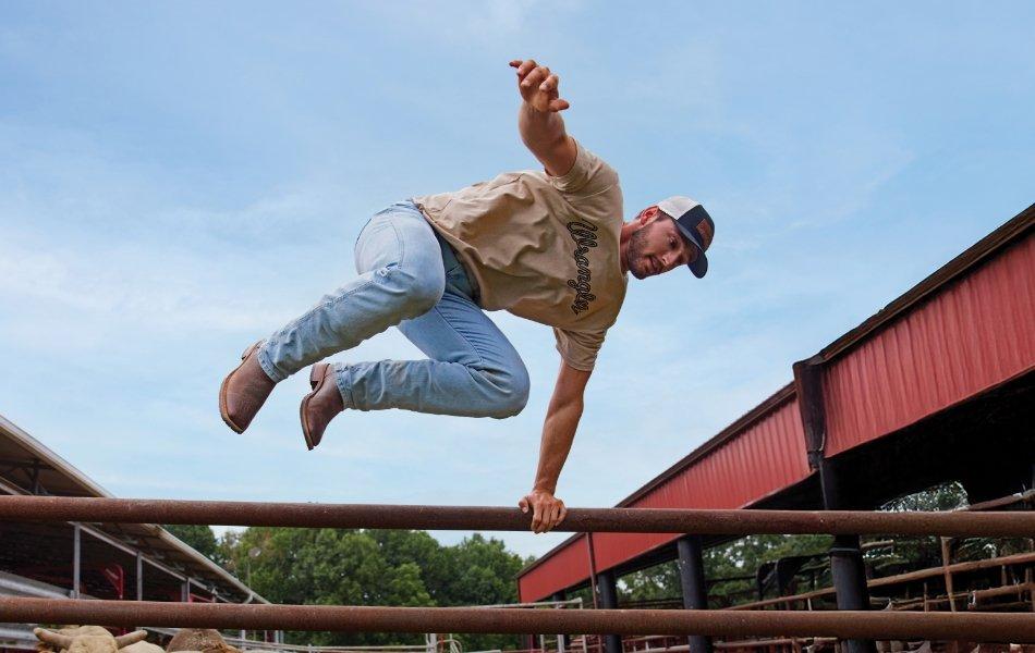 Man jumping over fence wearing Wrangler Toughlite jeans.