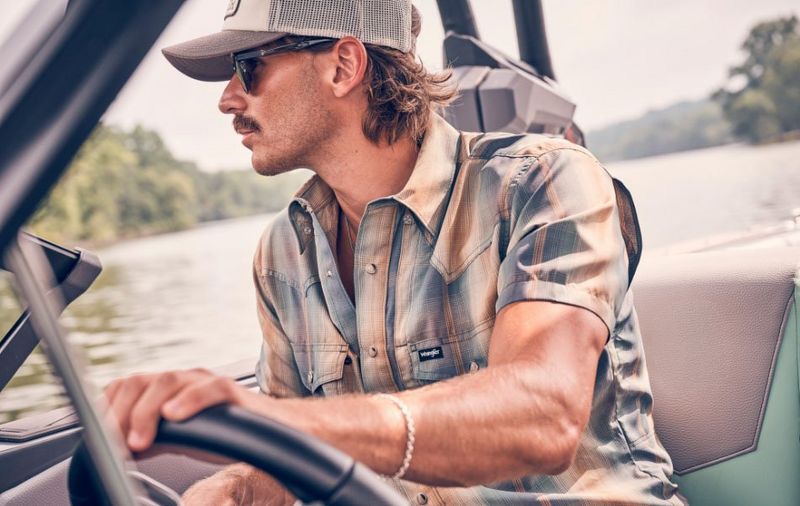 Guy driving a boat wearing a plaid shirt.