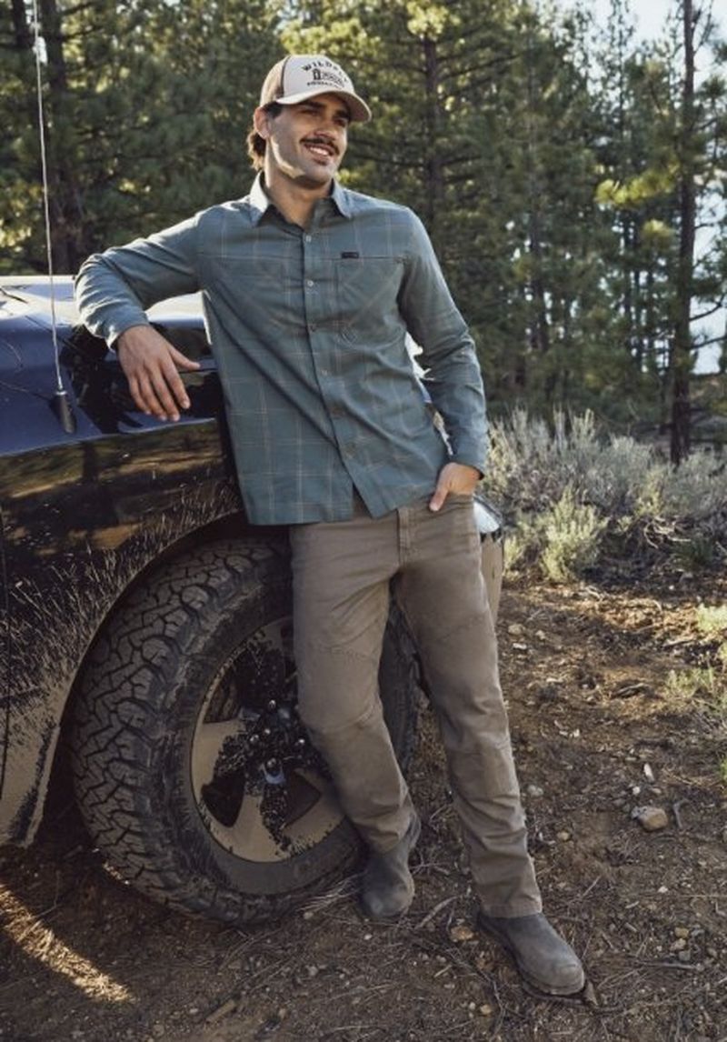 Guy leaning up against a muddy 4x4 wearing wrangler pants.