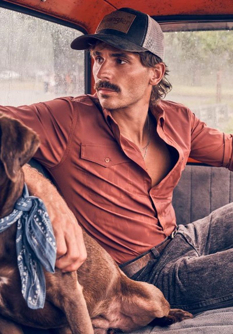 Guy leaning against a truck with a dog, wearing a performance shirt.