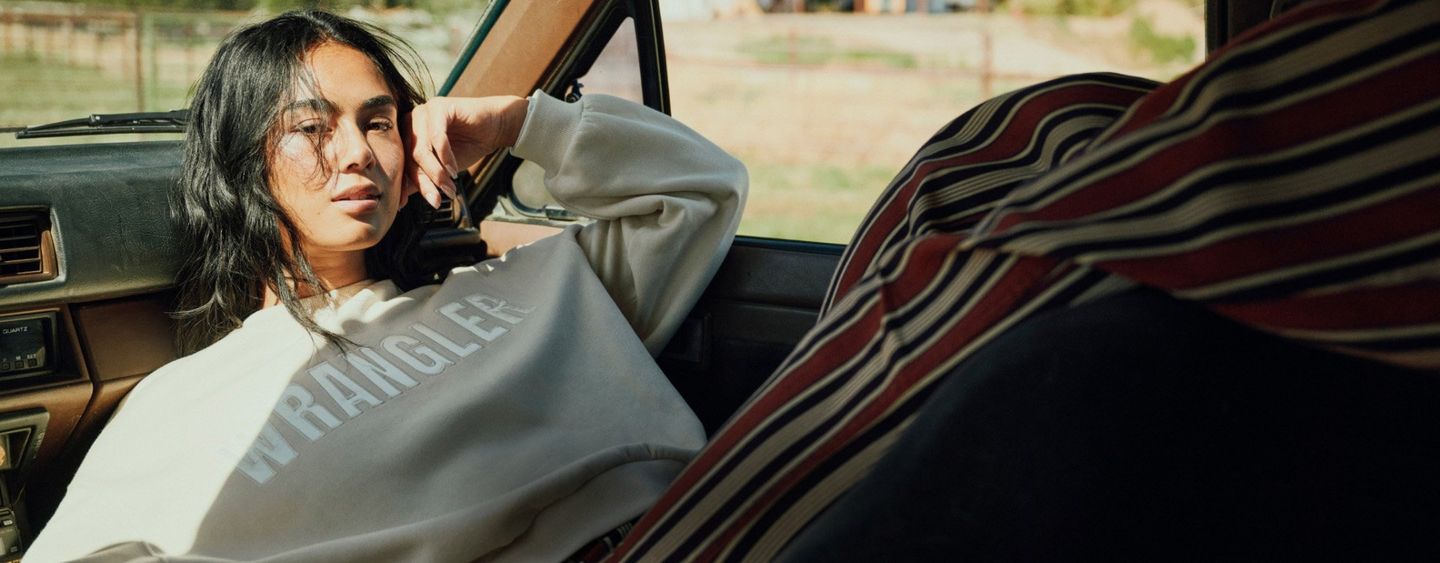 Woman wearing a wrangler sweatshirt, laying on the dask of a vintage truck.