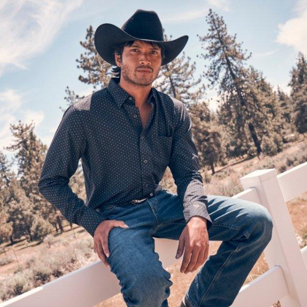 man sitting on truck bed wearing Wrangler and a cowboy hat looking into the camera