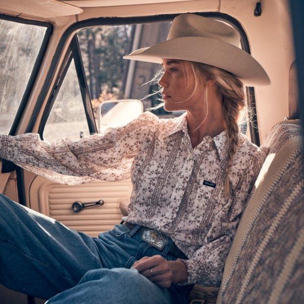 woman riding in a truck wearing Wrangler apparel and a cowboyhat looking out the window