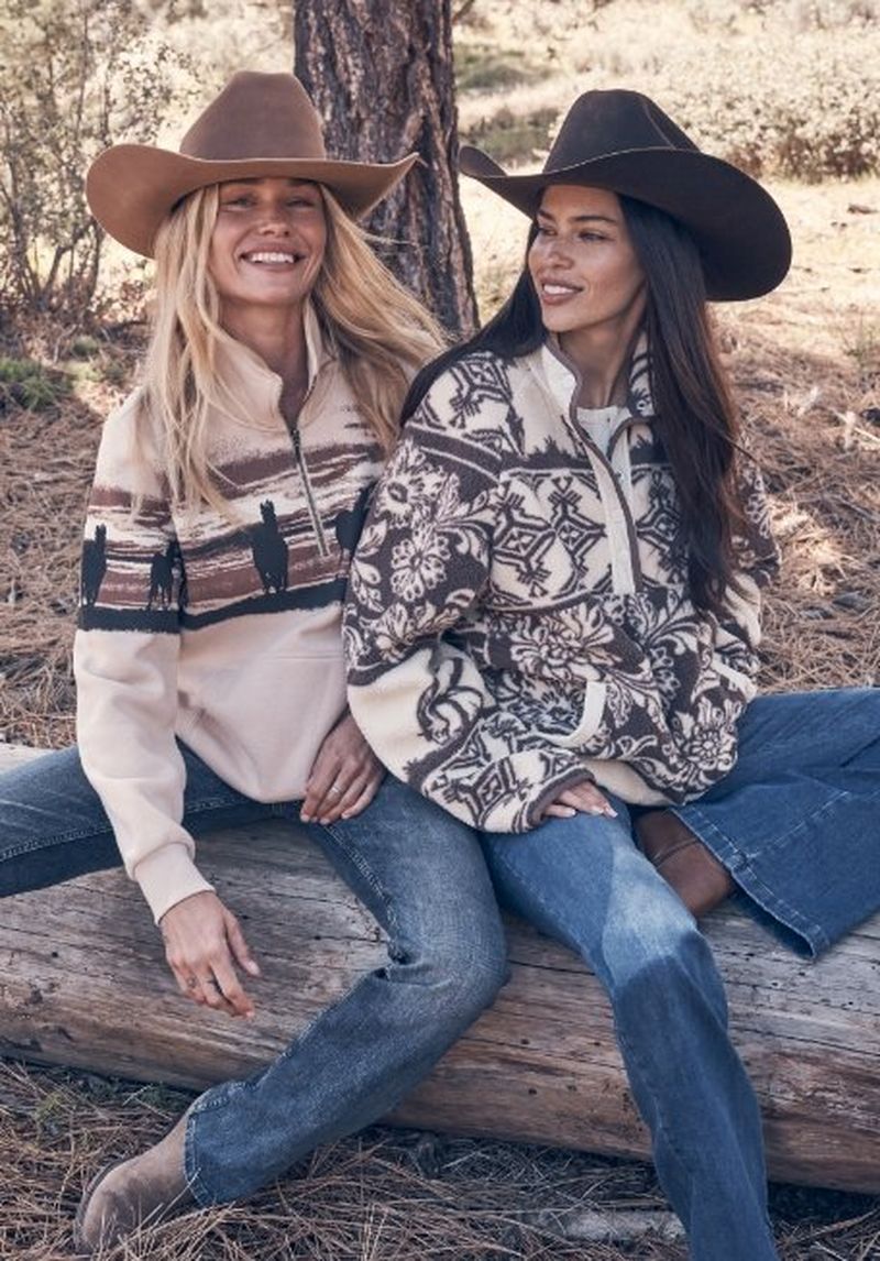 Two gals sitting outside on a log wearing pullovers - shop cozy gifts