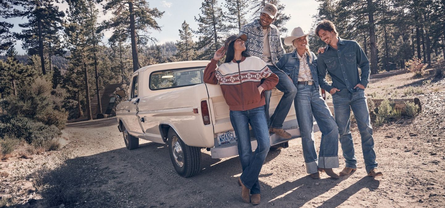 Guys and girls wearing fall clothes, gathered round a vintage truck in the woods. Shop Fall