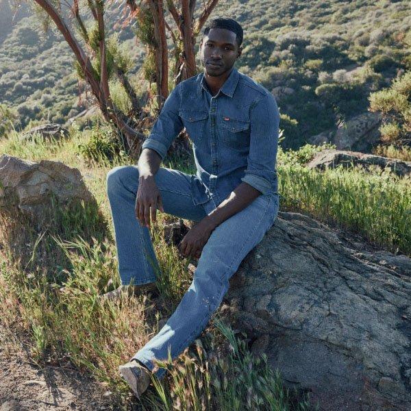 man sitting on a rock wearing denim on denim looking into the camera
