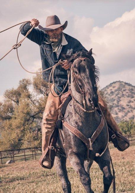 man riding a horse roping and wearing Wrangler apparel and a cowboy hat