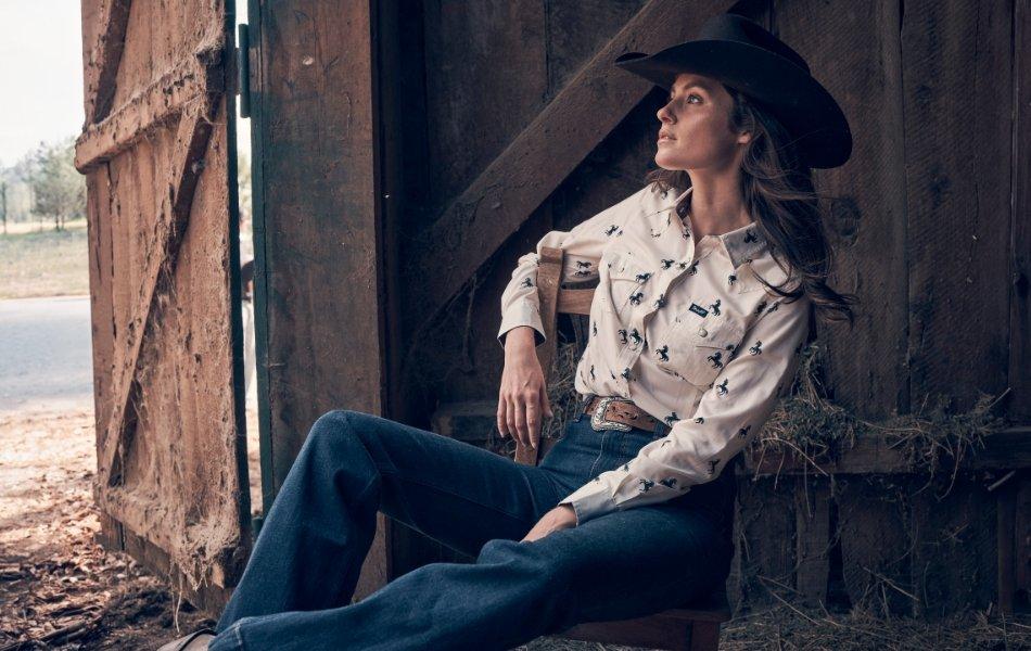 Woman sitting in a barn wearing Wrangler Ultimate Riding Jeans