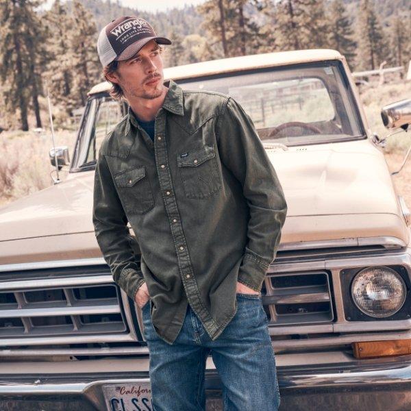 man leaning against a truck wearing Wrangler jeans.
