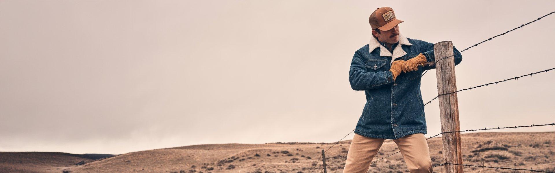 Guy wearing a sherpa jacket mending a cattle fence.