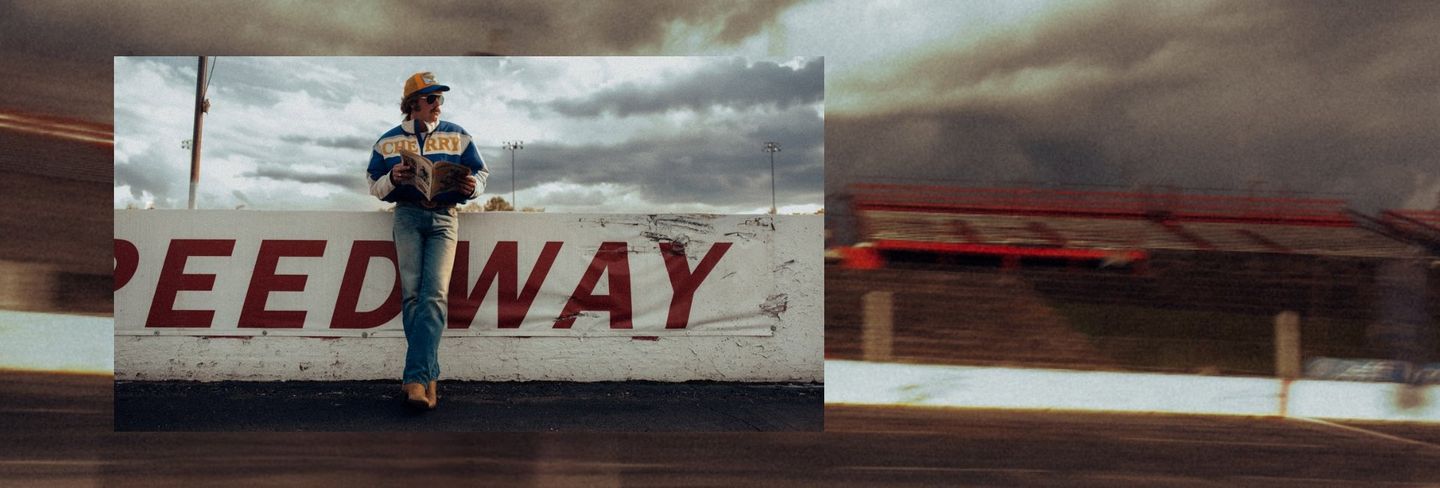 Guy leaning up against a racetrack barrier looking into the distance - Shop Wrangler x Cherry