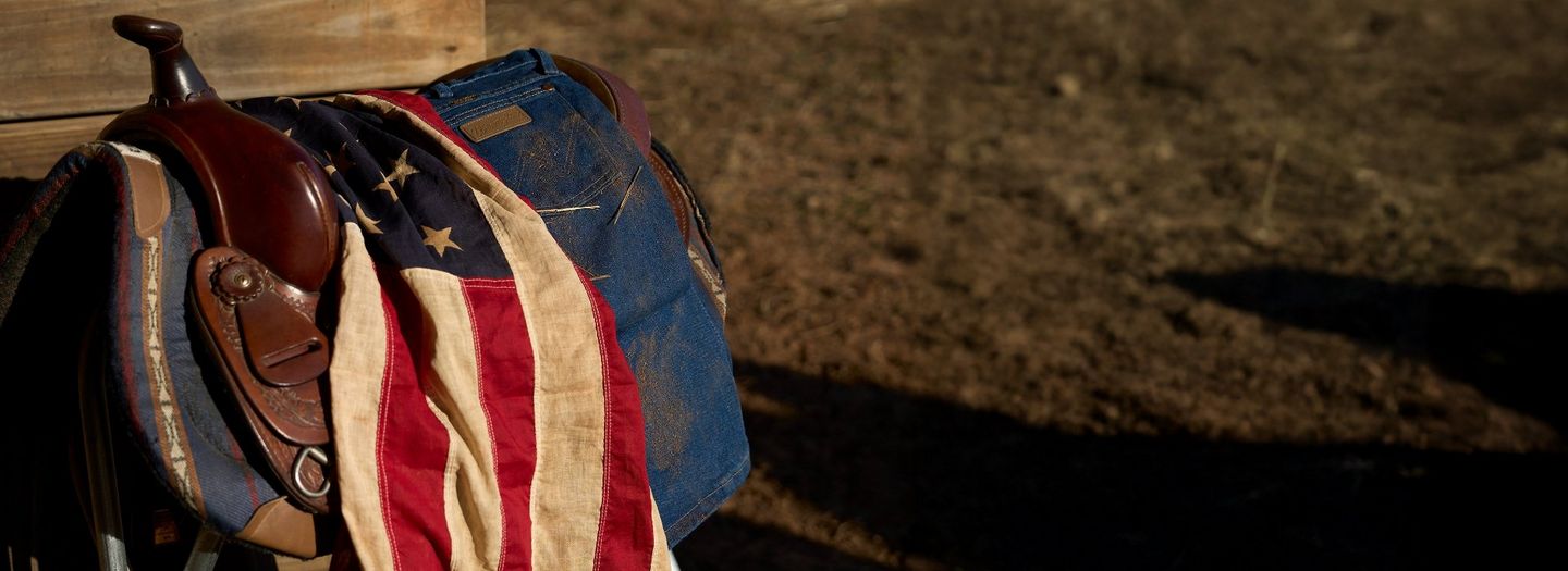 An american flag and pair of Wrangler jeans laying on a saddle.