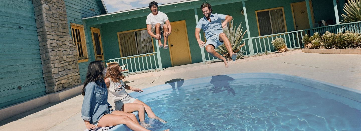2 guys and 2 girls by a pool, with the guys jumping in doing cannonballs. Shop Shorts