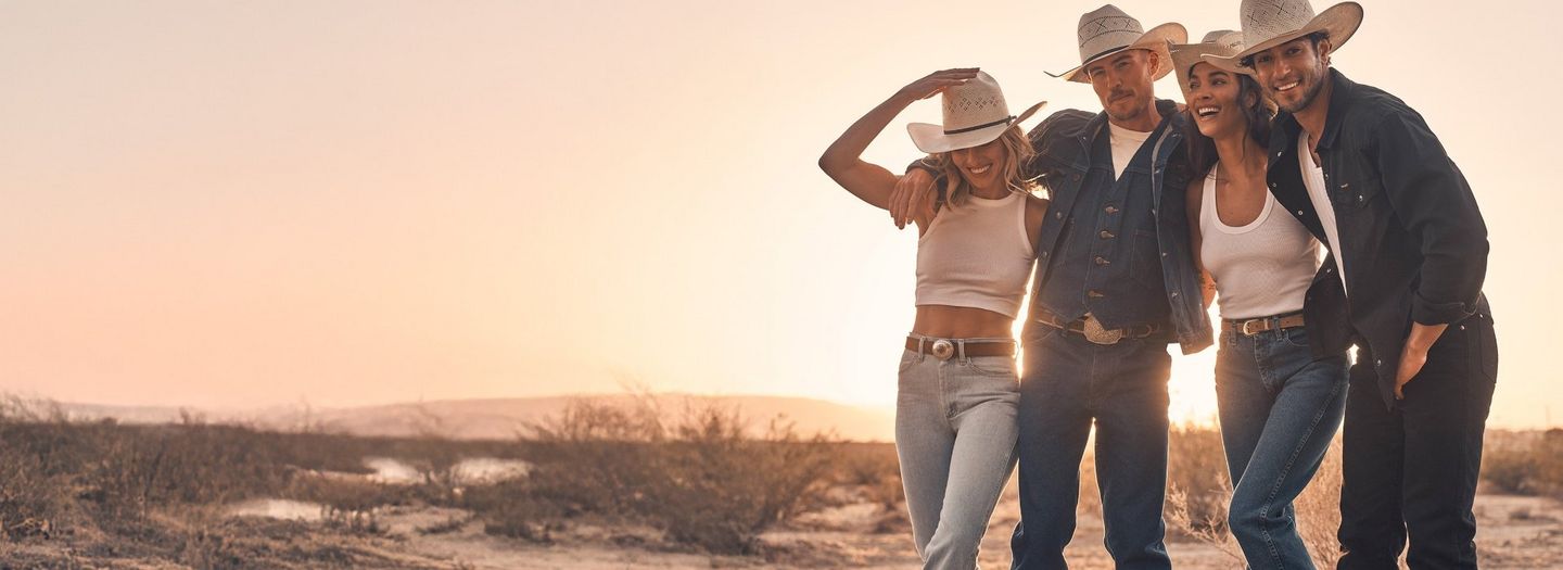 A group of men and women wearing cowboy hats as the sun goes down behind them.