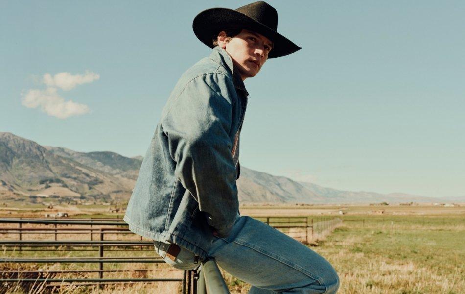 Guy wearing a denim jacket and jeans is sitting on rail