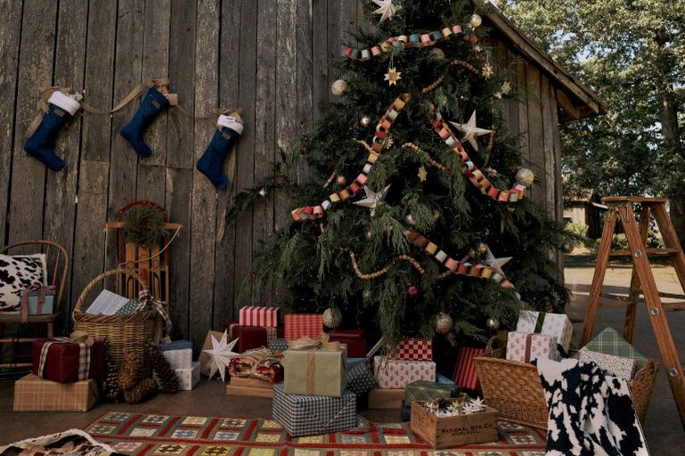 Decorated Christmas tree with wrapped gifts and denim stockings hanging on a barn wall