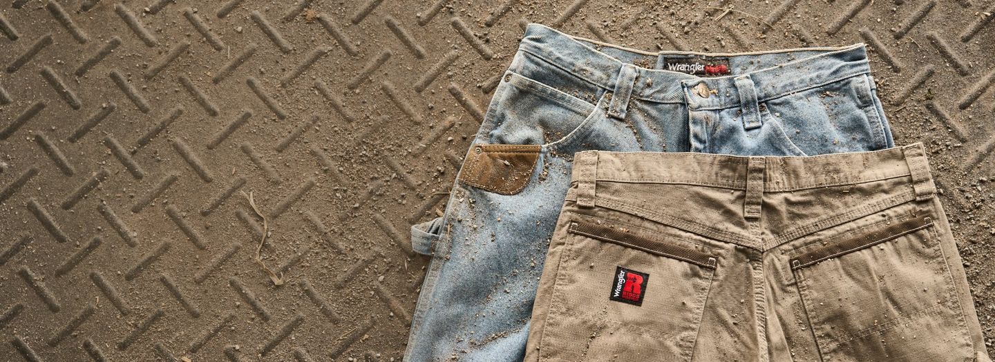 2 dirty Wrangler workwear pants laying on a textured floor.