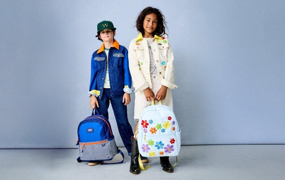 Two children modeling Wrangler STATE collection with decorative denim outfits and backpacks