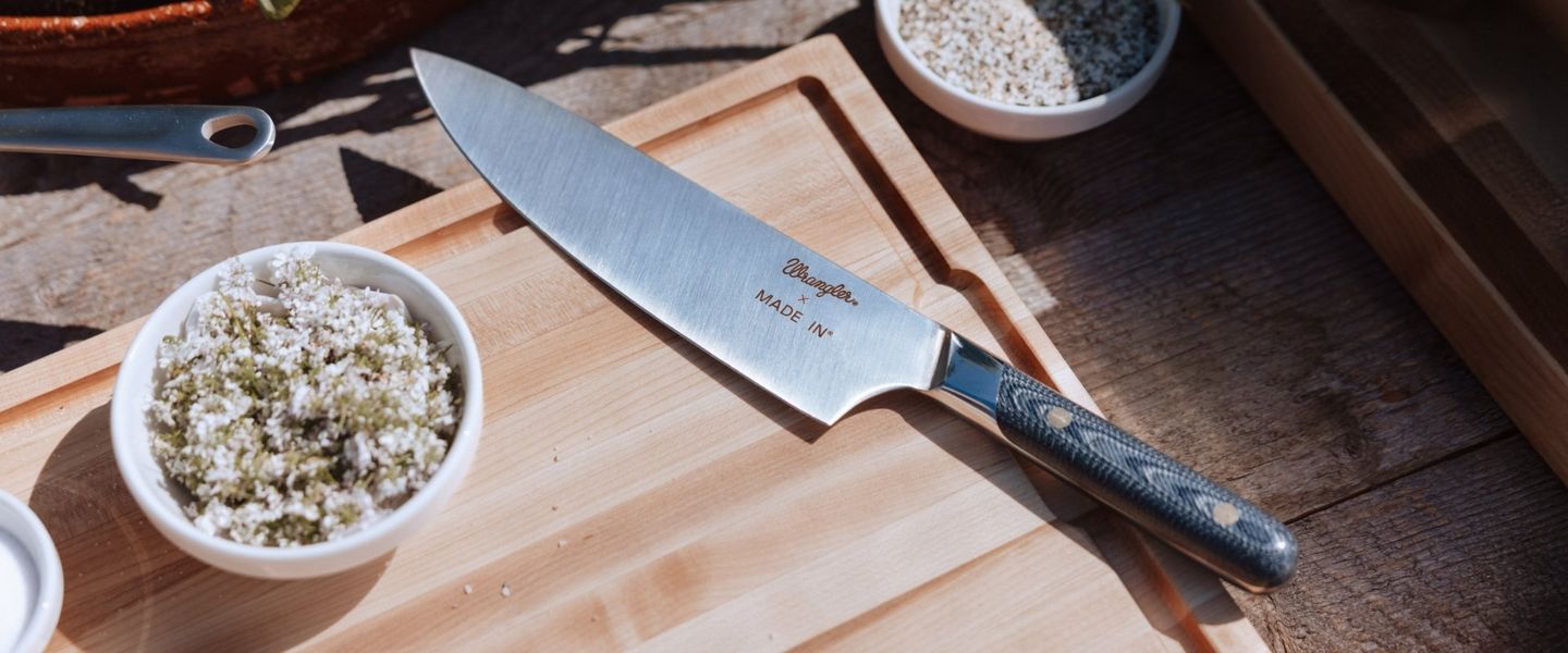 A knife sitting on a cutting board with "Wrangler x Made In" engraved on the blade.