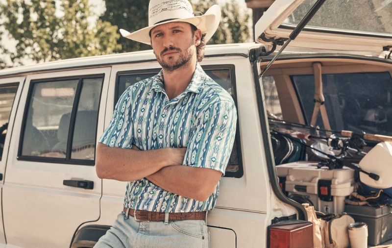 Guy leaned up against an old Jeep wearing a cowboy hat and polo - Shop Performance Polo