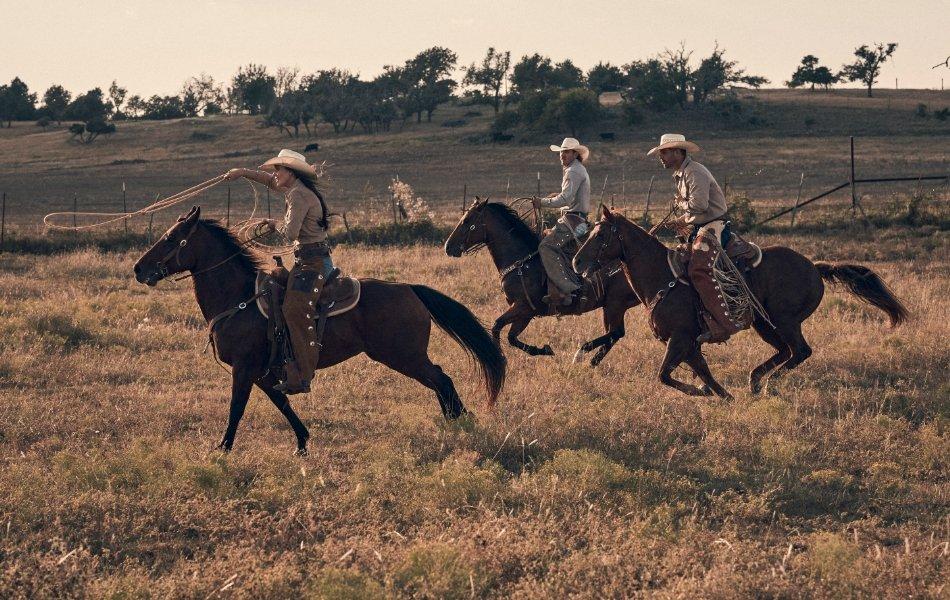 A woman and two men riding on horseback in a field.