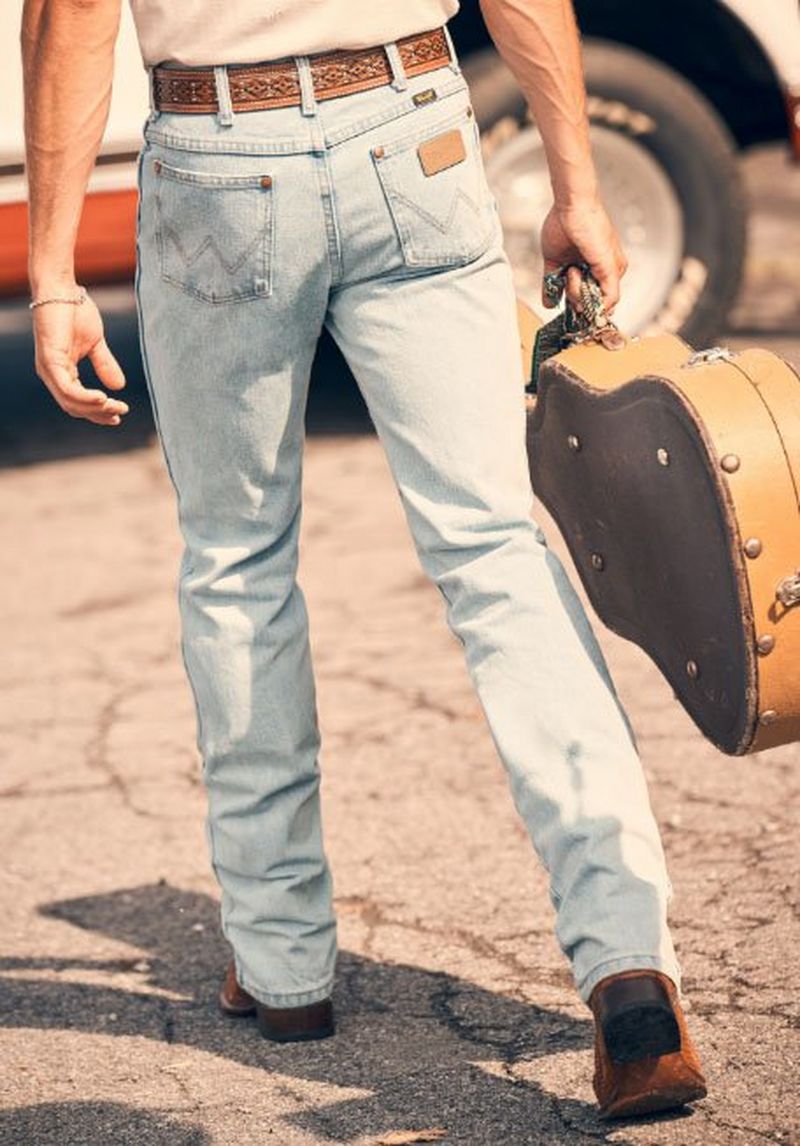 Guy walking away from camera holding a guitar case, wearing jeans.