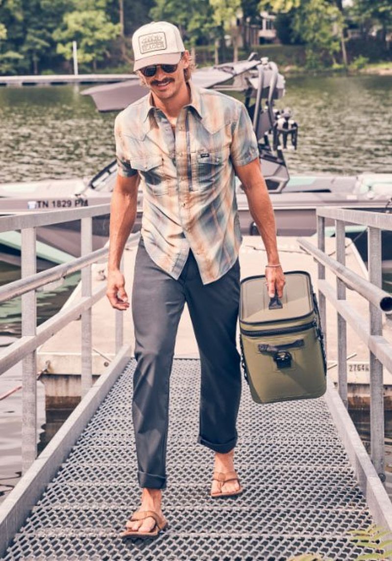 Guy walking on a dock carrying a cooler, wearing pants.