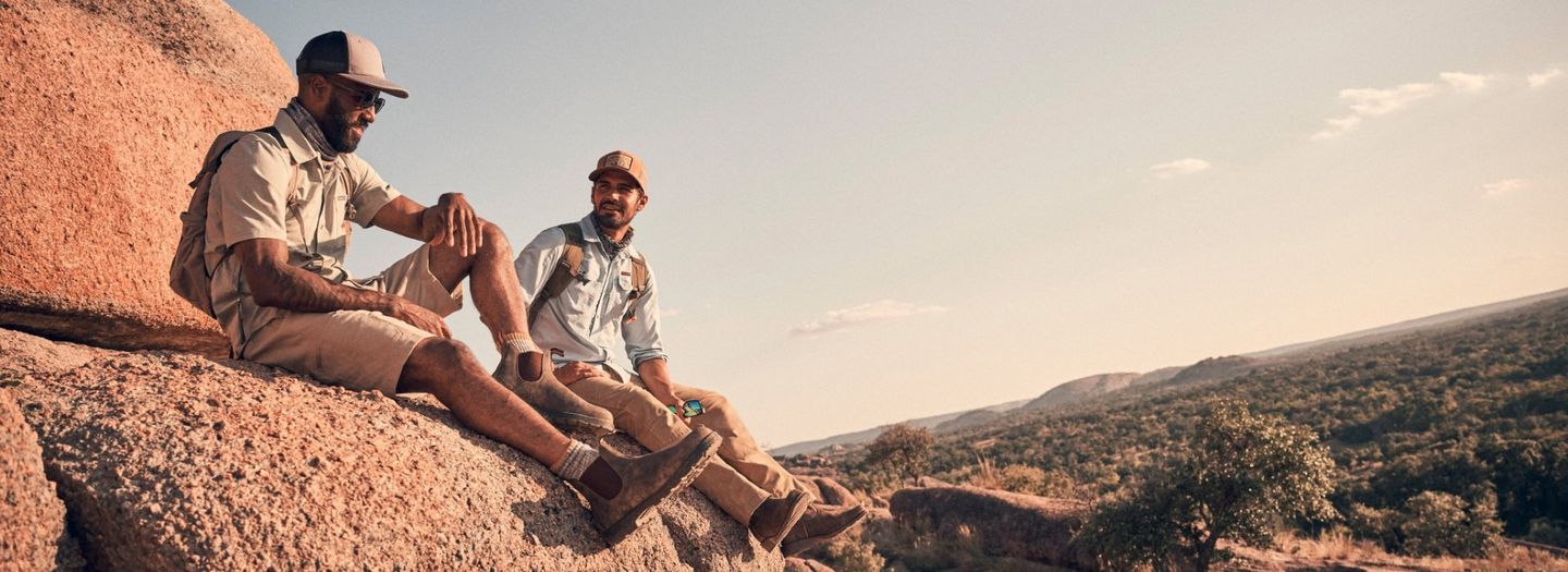 Two men sitting on a big rock in the desert.