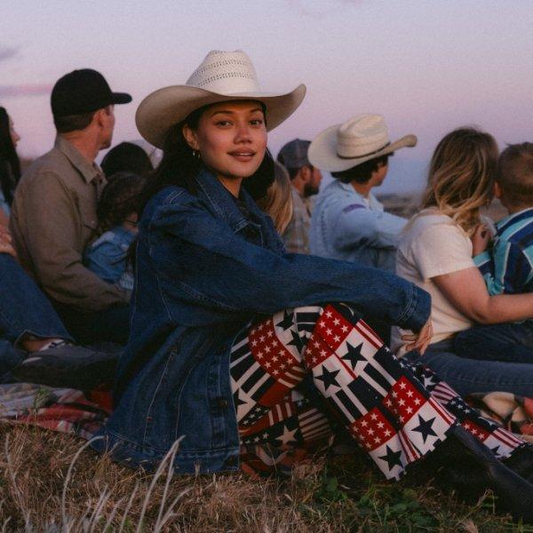 woman wearing red, white and blue patterned jeans and a cowboy hat looking into the camera