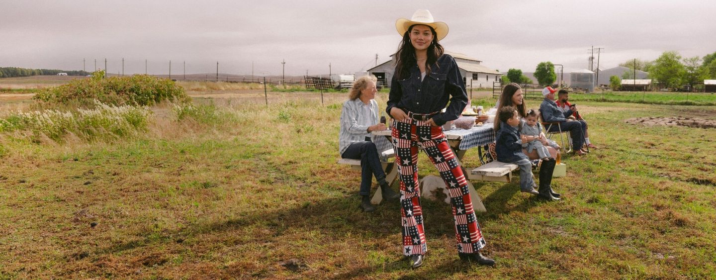 Girl standing at a picknick table wearing a cowboy hat and american flag pants