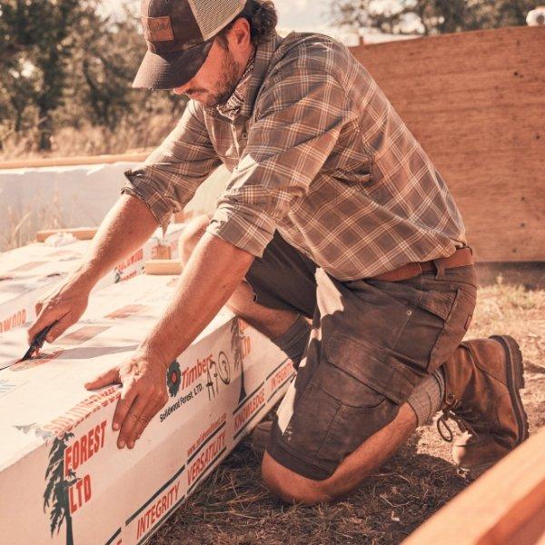 Man cutting insulation foam board outdoors during construction work.