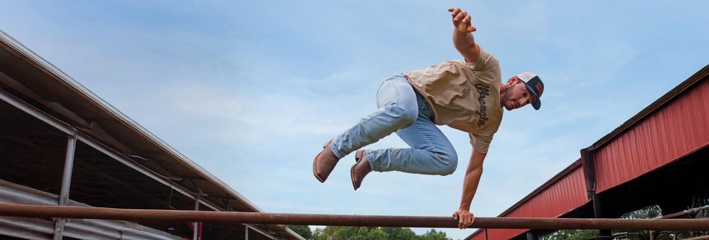 Guy wearing Wrangler Toughlite, jumping out of a cow pen.