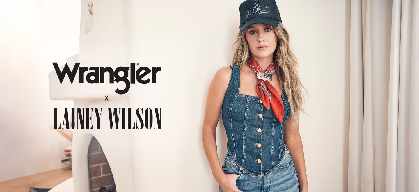 Lainey Wilson wearing a black hat, red handkerchief and denim vest